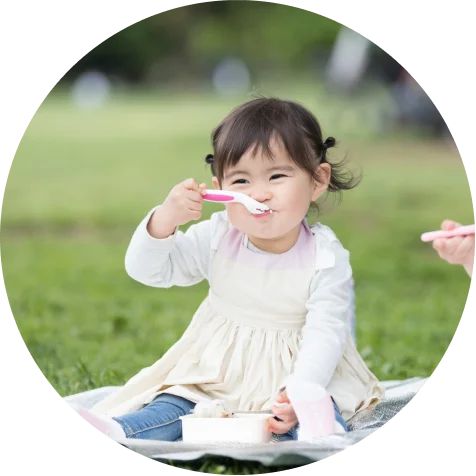 芝生の上でスプーンを持って食事を楽しむ幼児